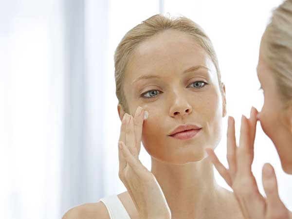Femme qui se regarde dans un miroir posant de la crème sur son visage